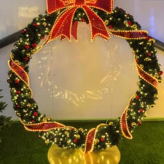 Giant decorative Christmas wreath with lights and a red bow on a stand.